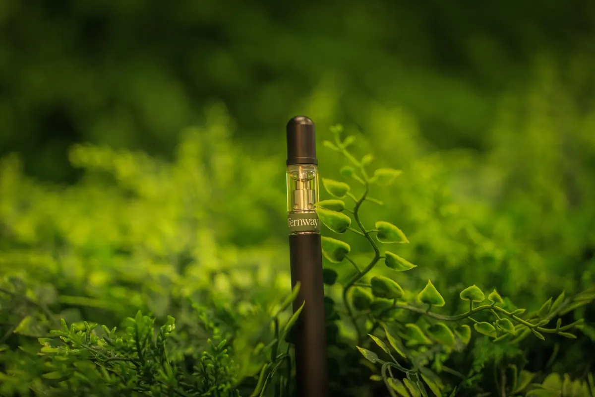 A vape pen standing upright among green leaves