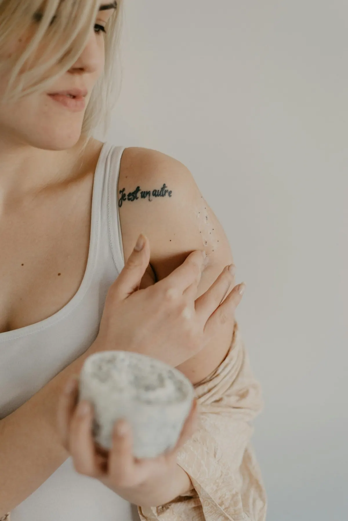 A woman holding a jar of lotion with her hand resting on her shoulder