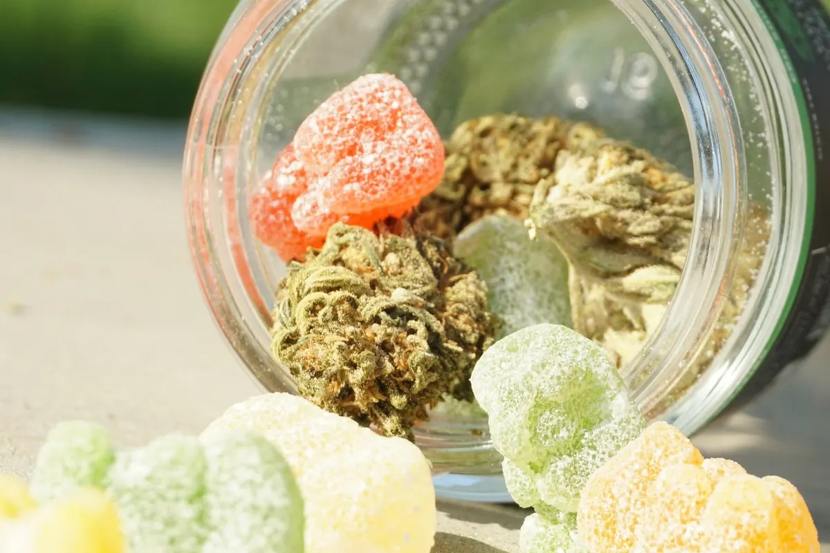 Gummies and cannabis flower spilling out of a glass jar